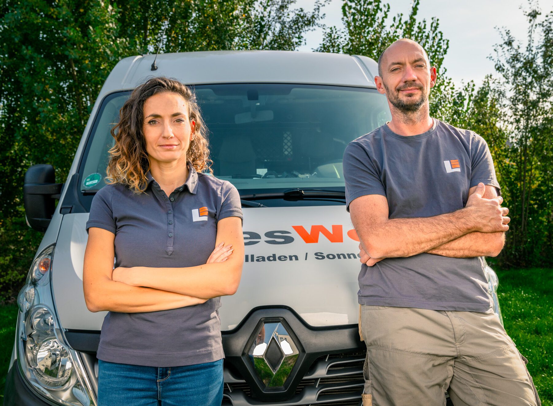 Ein Mann und eine Frau lehnen an der Motohaube eines Busses. Auf der Motohaube steht der Schriftzug 'Landeswerk'